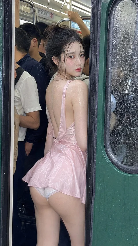 A person in a pale pink outfit looks back toward the camera at the open doorway of a crowded train.